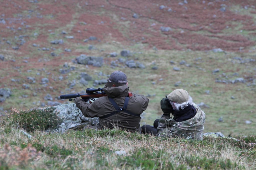 Two hunters surveying landscape with scopes.
