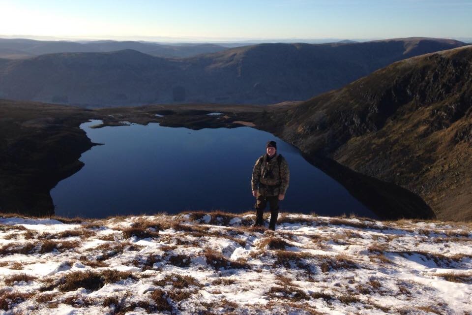 Person standing on snowy hill overlooking mountain lake.