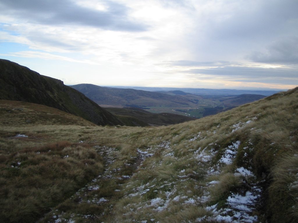 Snowy hills overlooking vast landscape under cloudy skies.