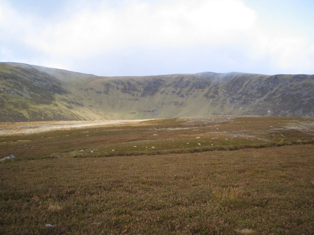 Hilly landscape with grassy terrain and cloudy sky.