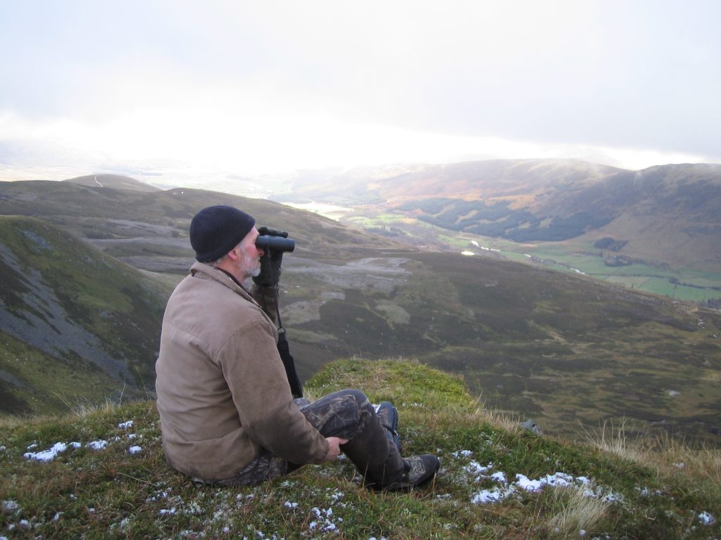 Man observing landscape with binoculars on hillside